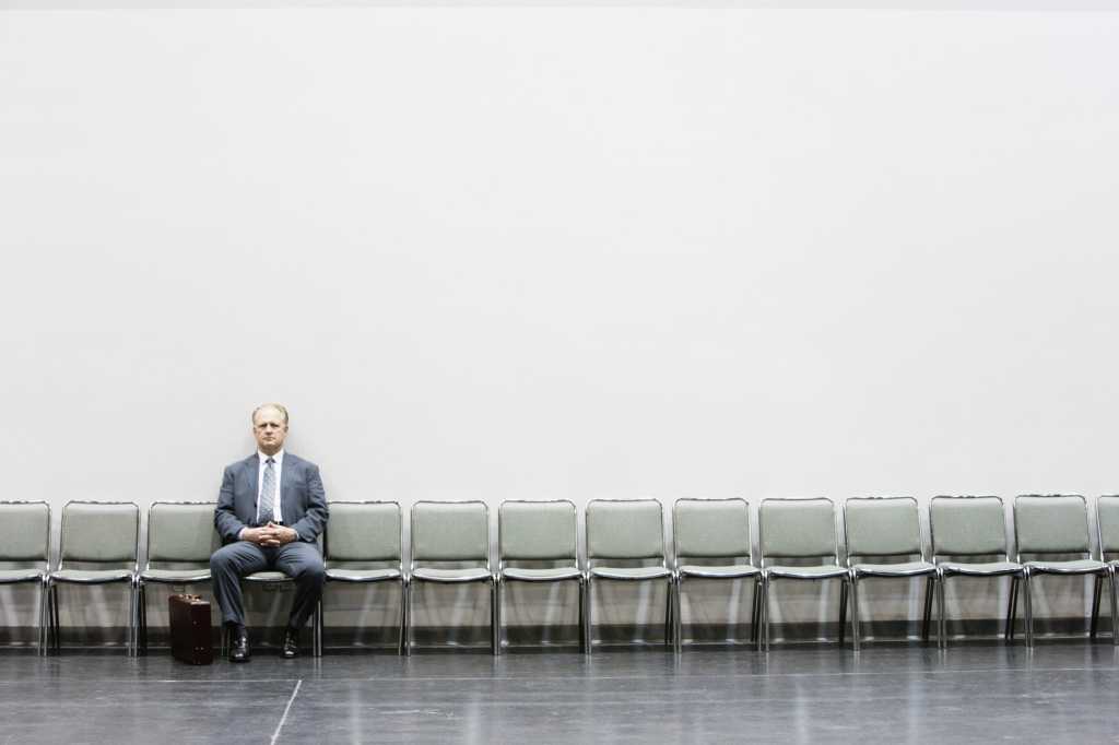 Man in blue suit waiting for interview on long row of empty chairs against white wall