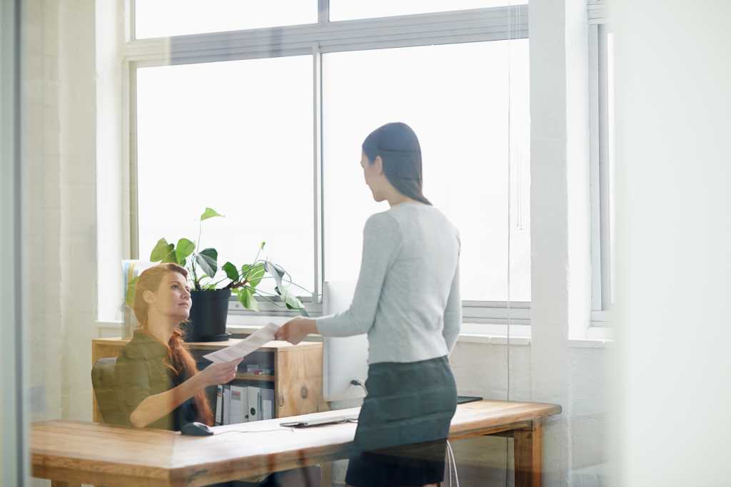 Documents, resignation letter and business women in office for quitting, termination and unemployment note. Corporate, discussion and female worker giving manager paperwork to resign in workplace